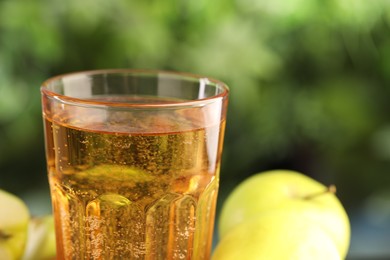 Photo of Delicious cider in glass and apples on blurred background, closeup