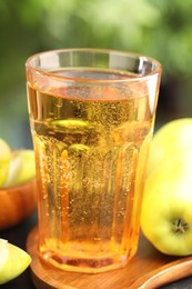 Photo of Delicious cider in glass and apples on table outdoors, closeup