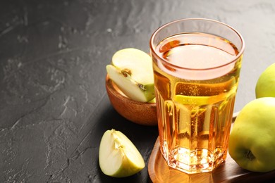 Photo of Delicious cider in glass and apples on black table, closeup. Space for text