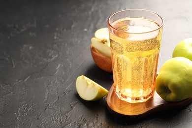 Photo of Delicious cider in glass and apples on black table. Space for text