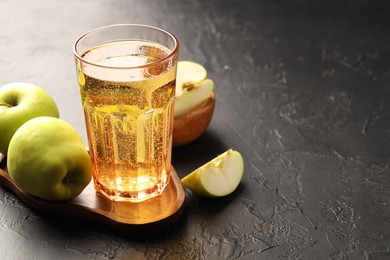 Photo of Delicious cider in glass and apples on black table. Space for text