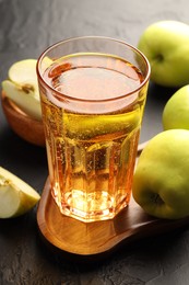 Photo of Delicious cider in glass and apples on black table, closeup