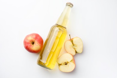 Photo of Delicious cider in glass bottle and apples on white background, flat lay