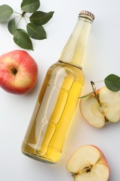 Photo of Delicious cider in glass bottle, apples and green leaves on white background, flat lay