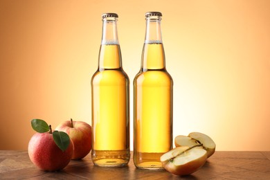 Photo of Delicious cider in glass bottles and apples on wooden table against orange gradient background