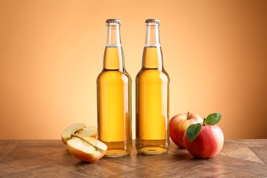 Photo of Delicious cider in glass bottles and apples on wooden table against orange gradient background