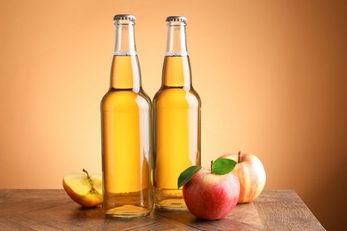 Photo of Delicious cider in glass bottles and apples on wooden table against orange gradient background