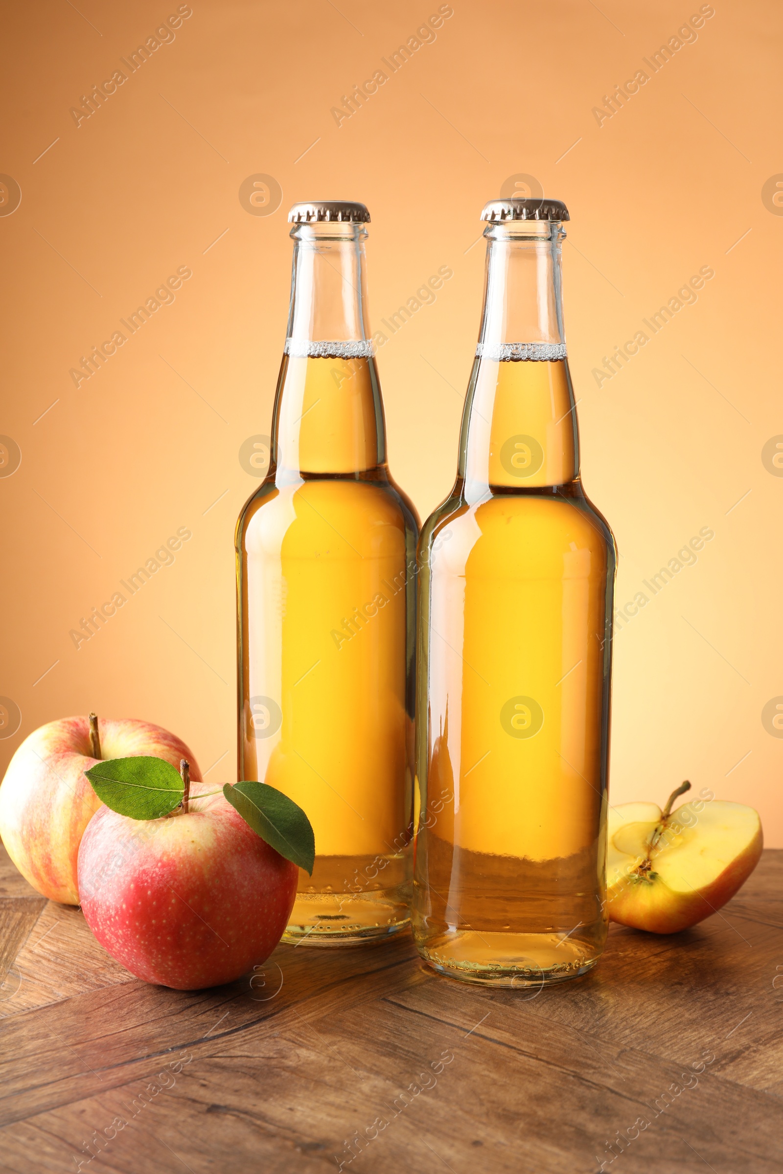 Photo of Delicious cider in glass bottles and apples on wooden table against orange gradient background