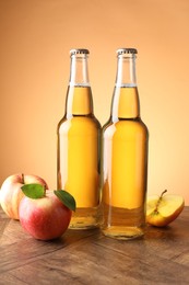 Photo of Delicious cider in glass bottles and apples on wooden table against orange gradient background