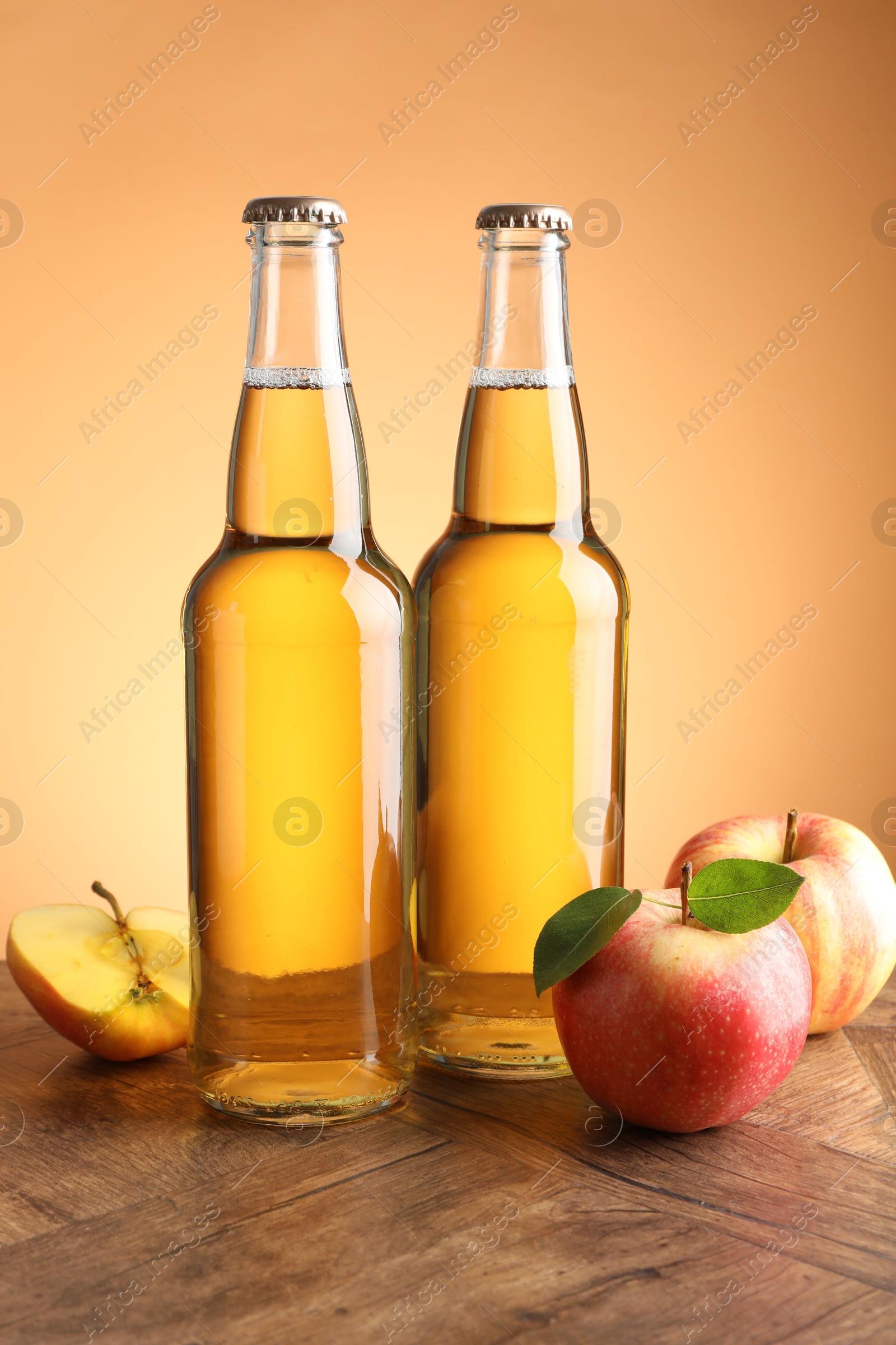 Photo of Delicious cider in glass bottles and apples on wooden table against orange gradient background