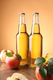 Photo of Delicious cider in glass bottles and apples on wooden table against orange gradient background