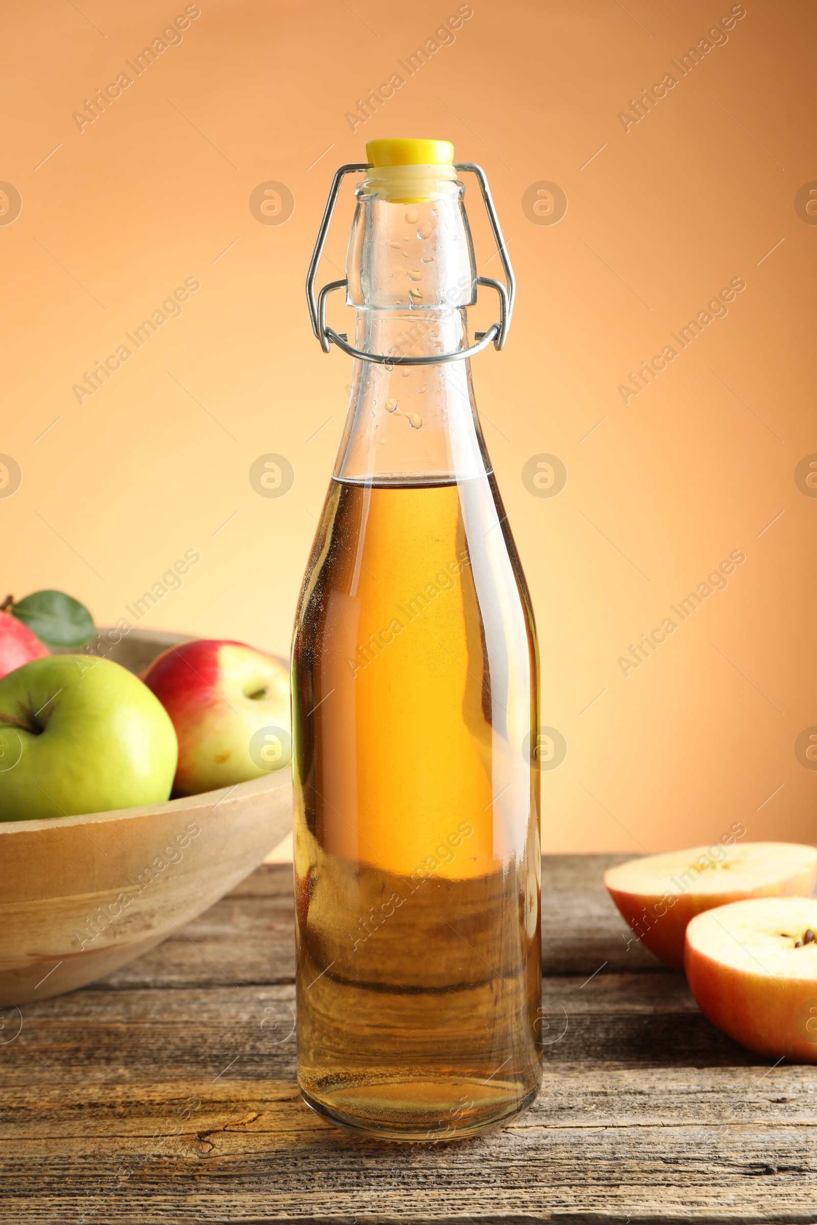 Delicious cider in glass bottle and apples on wooden table against orange gradient background Photo of Delicious cider in glass bottle and apples on wooden table against orange gradient background