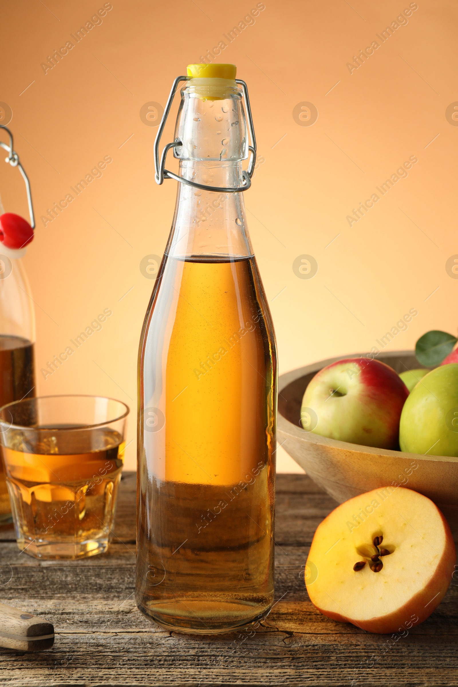 Delicious cider in bottle, glass and apples on wooden table against orange gradient background, closeup Photo of Delicious cider in bottle, glass and apples on wooden table against orange gradient background, closeup