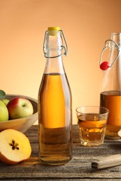 Photo of Delicious cider in bottles, glass and apples on wooden table against orange gradient background, closeup