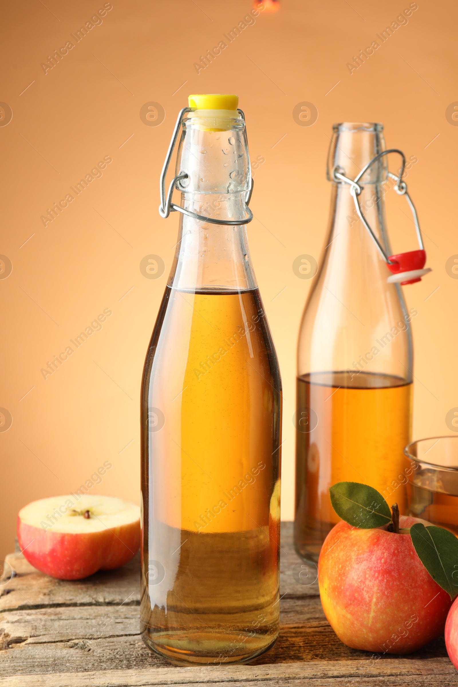Photo of Delicious cider in bottles, glass and apples on wooden table against orange gradient background, closeup