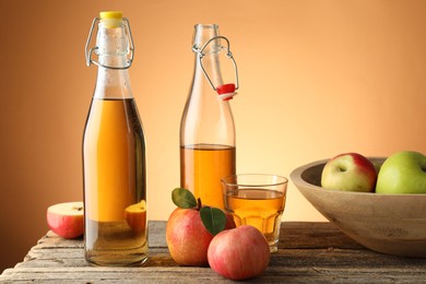 Photo of Delicious cider in bottles, glass and apples on wooden table against orange gradient background