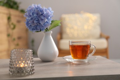 Photo of Vase with beautiful flower, tea and burning candle on table in room