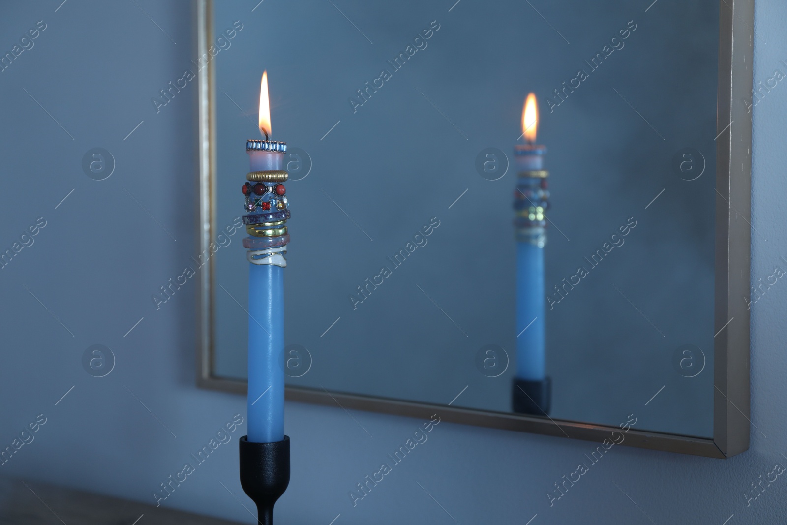 Photo of Burning candle with different rings in front of mirror