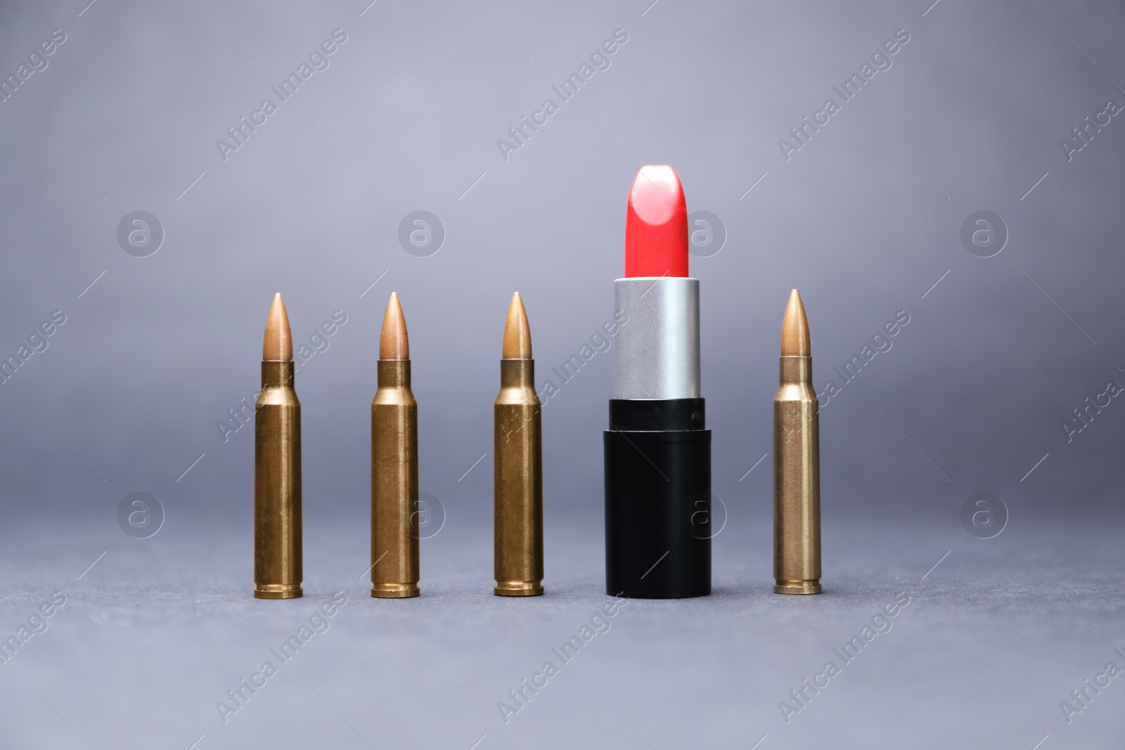Photo of Red lipstick among bullets on grey background