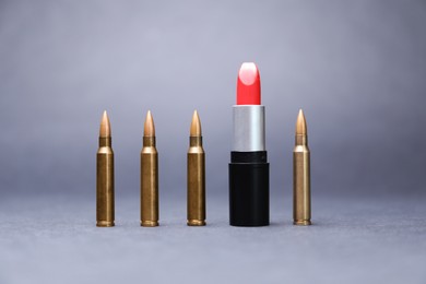 Photo of Red lipstick among bullets on grey background