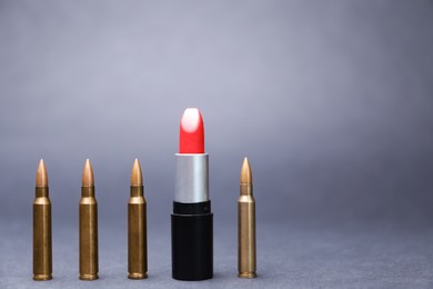 Photo of Red lipstick among bullets on grey background. Space for text