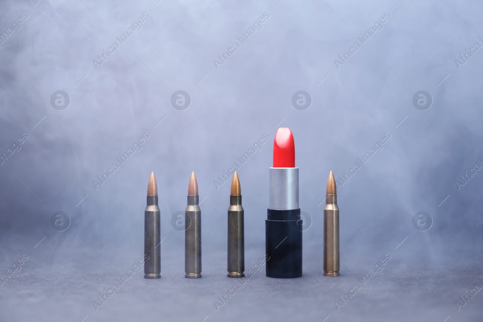 Photo of Red lipstick among bullets in smoke on grey background