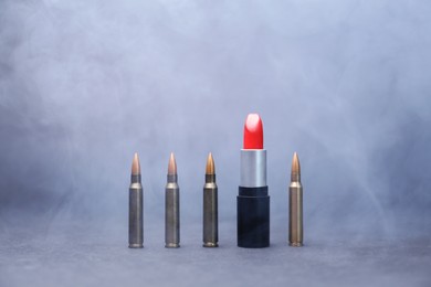 Photo of Red lipstick among bullets in smoke on grey background