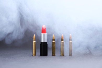 Photo of Red lipstick among bullets in smoke on grey background