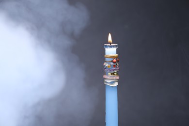 Photo of Burning candle with different rings and smoke against grey background
