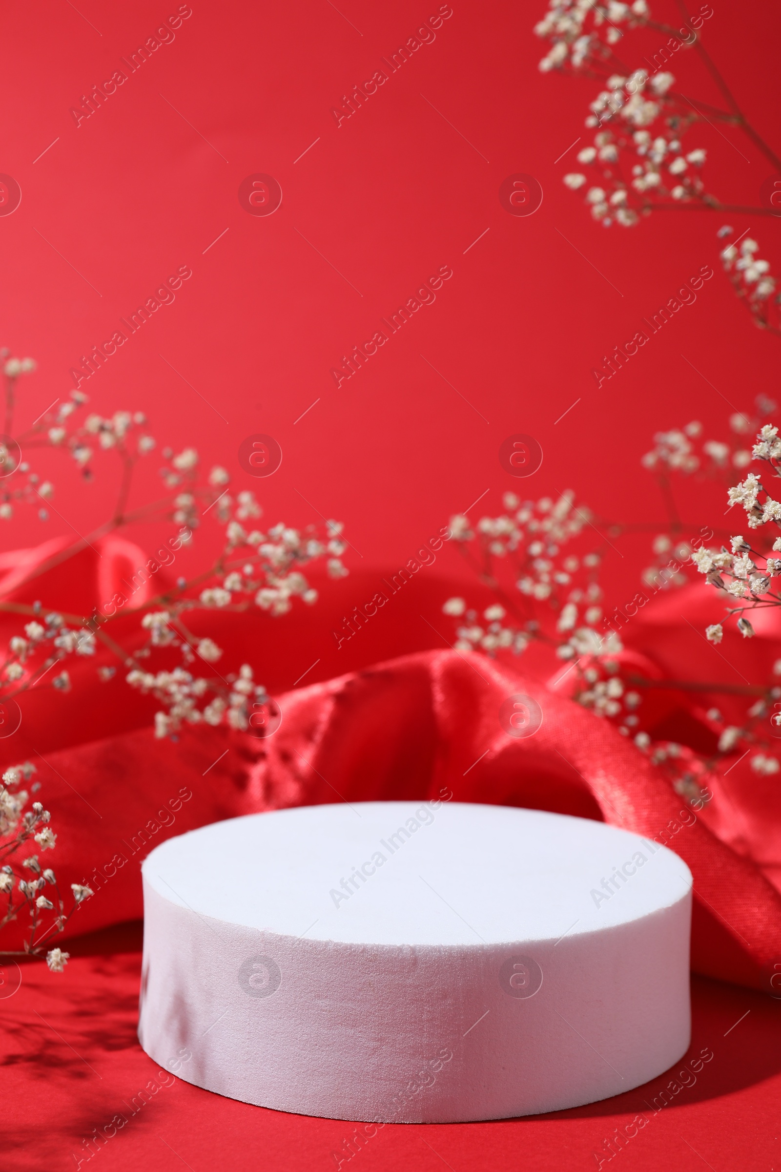 Photo of Promotion. Podium for product presentation, fabric and gypsophila flowers on red background, closeup
