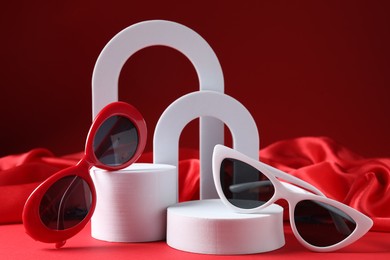 Photo of Promotion. Stylish sunglasses and podiums on red background