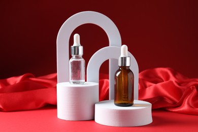 Photo of Promotion. Bottles of cosmetic products, podiums and fabric on red background