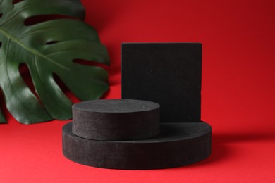 Photo of Promotion. Different podiums for product presentation and monstera leaf on red background