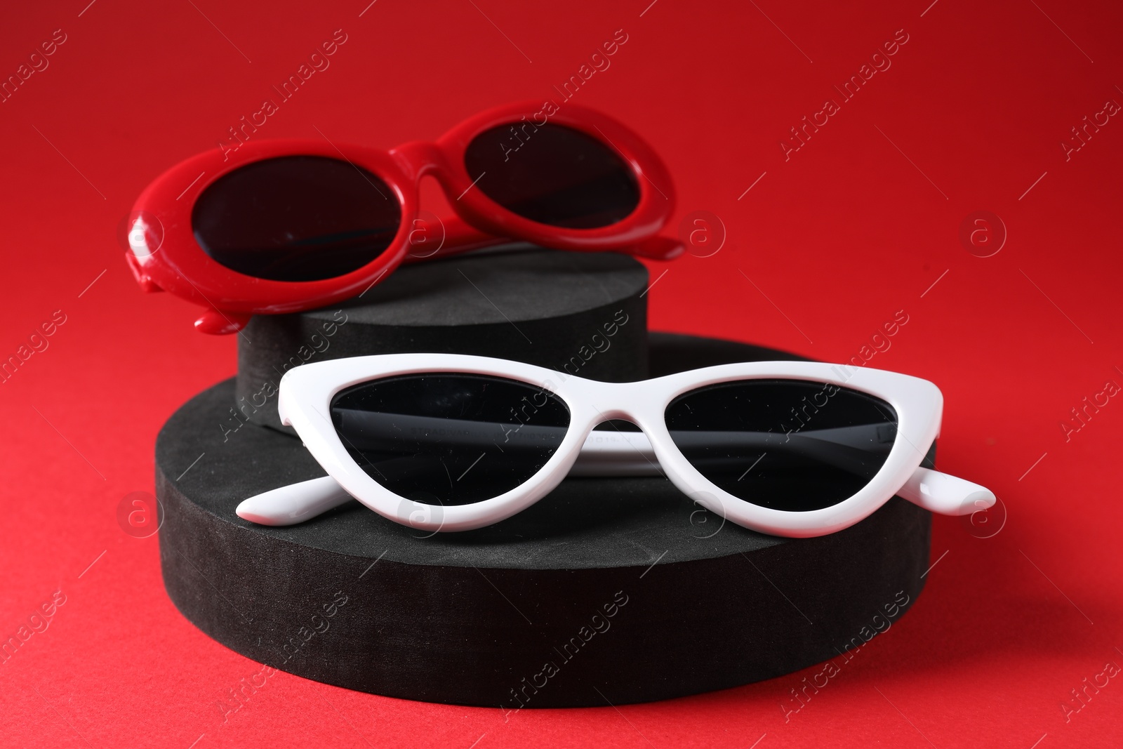 Photo of Promotion. Stylish sunglasses and podiums on red background