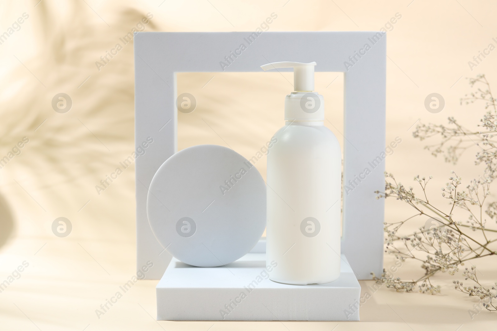 Photo of Promotion. Bottle of cosmetic product, geometric figures and gypsophila flowers on beige background