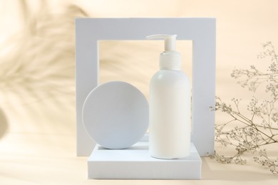Photo of Promotion. Bottle of cosmetic product, geometric figures and gypsophila flowers on beige background