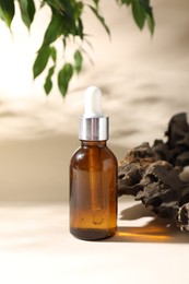 Photo of Promotion. Bottle of cosmetic product, green leaves and driftwood on beige background, closeup