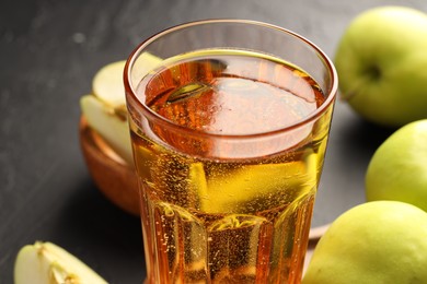 Photo of Delicious cider in glass and apples on black table, closeup