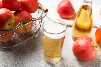 Photo of Delicious cider in glass, bottle and apples on light grey table, closeup