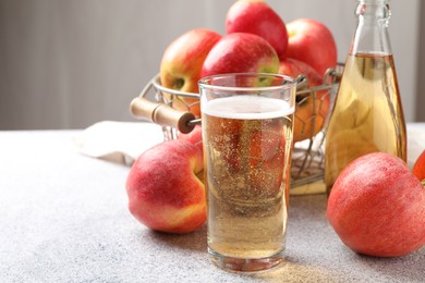 Photo of Delicious cider in glass, bottle and apples on light grey table, closeup. Space for text