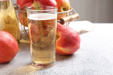 Photo of Delicious cider in glass, bottle and apples on light grey table, closeup. Space for text