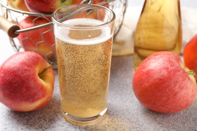 Photo of Delicious cider in glass, bottle and apples on light grey table, closeup