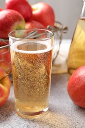 Photo of Delicious cider in glass and apples on light grey table, closeup