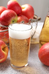 Photo of Delicious cider in glass and apples on light grey table, closeup