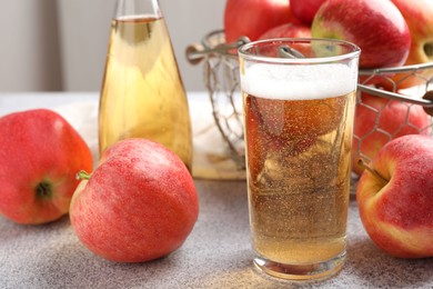 Photo of Delicious cider in glass, bottle and apples on light grey table, closeup