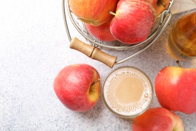 Photo of Delicious cider in glass, bottle and apples on light grey table, flat lay. Space for text