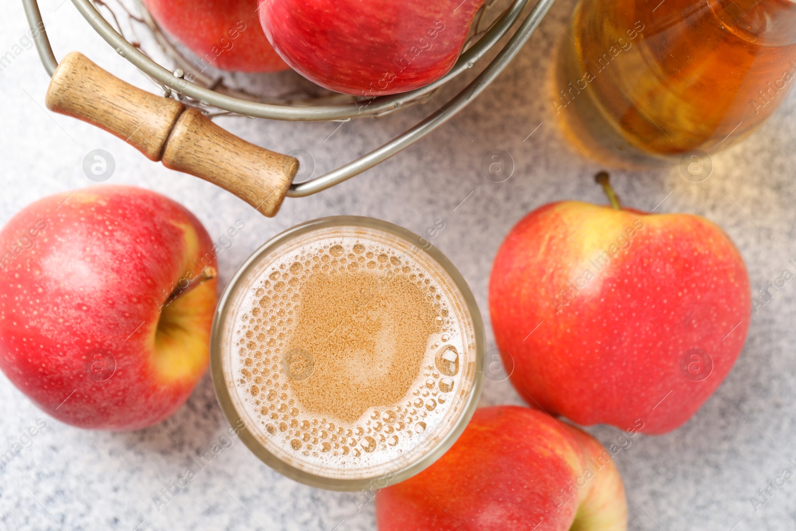 Photo of Delicious cider in glass, bottle and apples on light grey table, flat lay