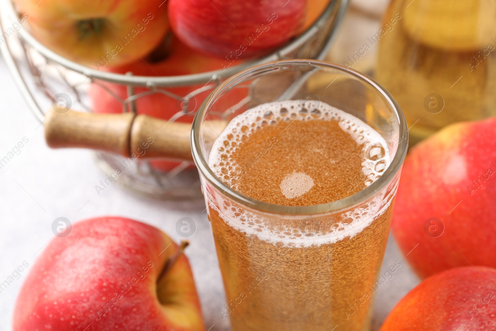 Photo of Delicious cider in glass and apples on light grey table, closeup