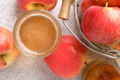 Photo of Delicious cider in glass and apples on light grey table, flat lay