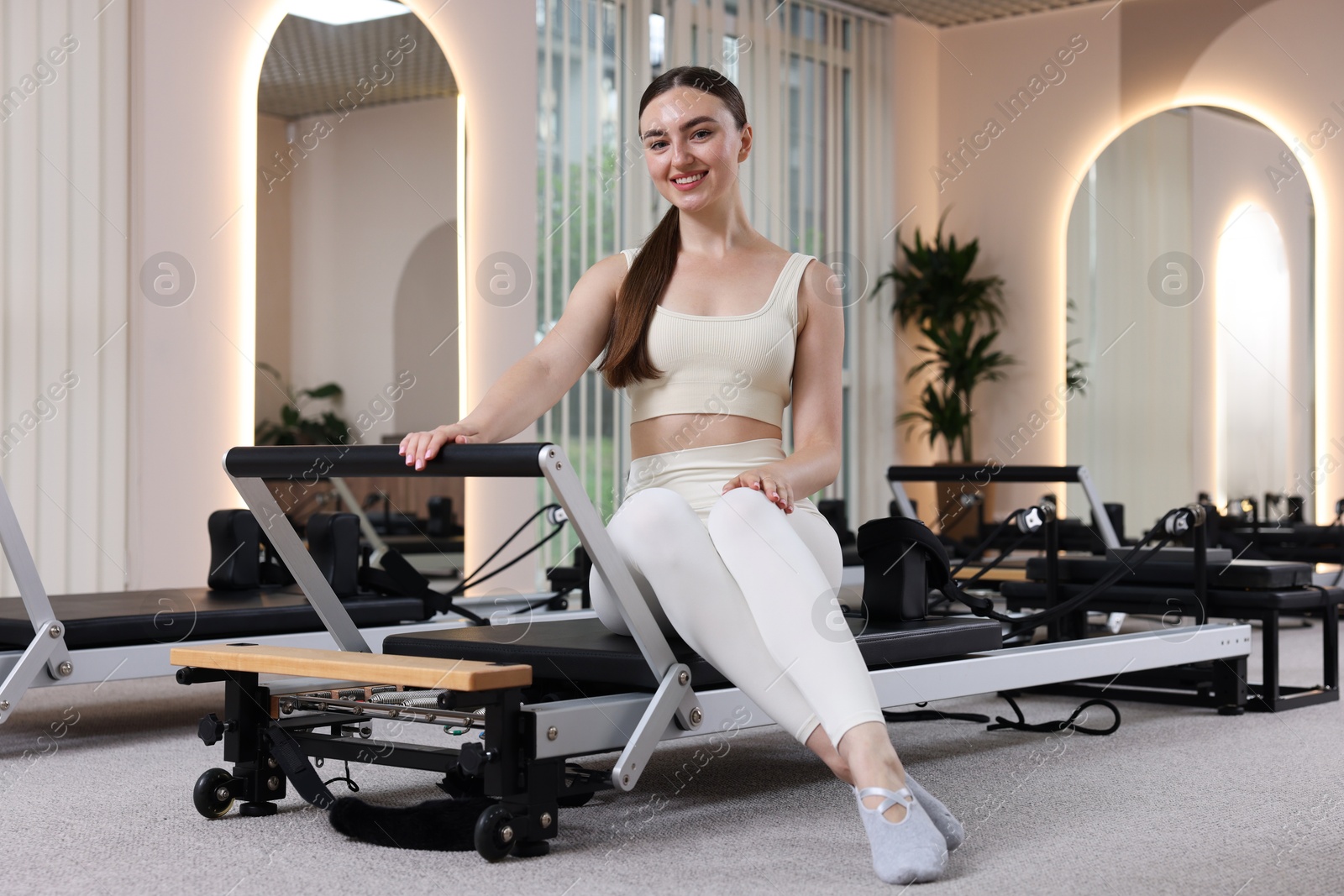 Woman sitting on reformer in pilates studio Photo of Woman sitting on reformer in pilates studio